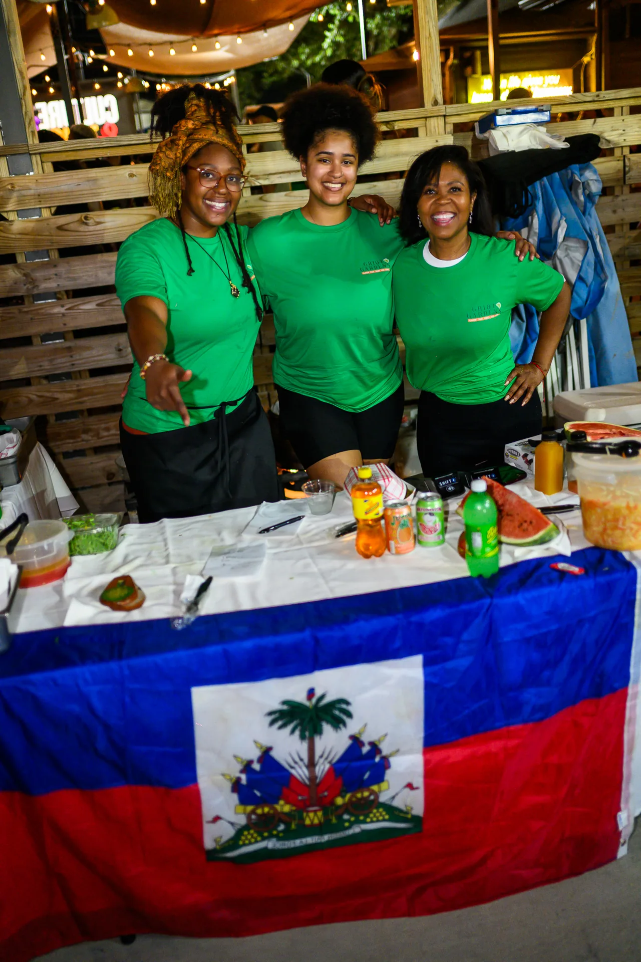 Smiling vendors behind a table displaying the Haitian flag at Culture & Tings.